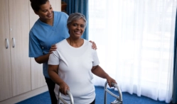 A female caregiver assisting a senior woman to walk