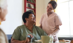 A female caregiver and a senior woman looking at each other smiling