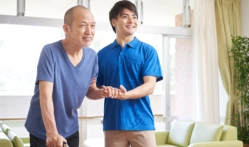 A male assisting a senior man to walk