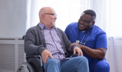 A senior man sitting on a wheelchair with a man caregiver