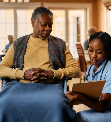 A female caregiver showing something to a senior man sitting on a wheelchair