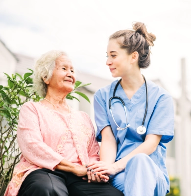 A female caregiver and a senior woman looking at each other smiling