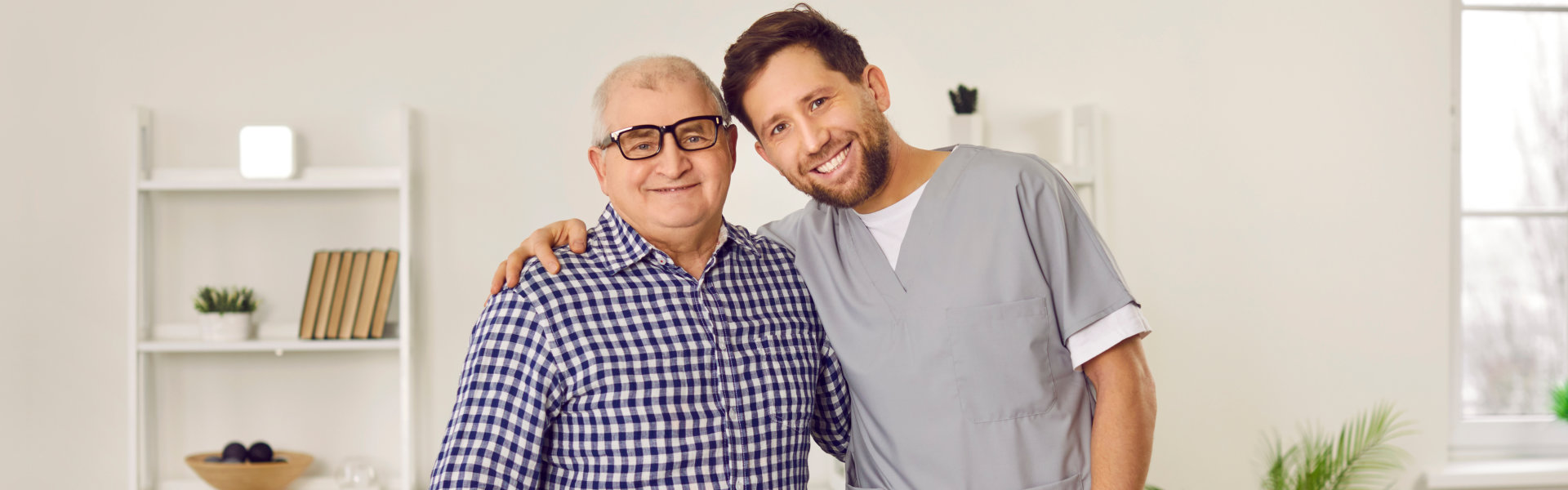 A male caregiver and a senior man putting their arms on each other's shoulders