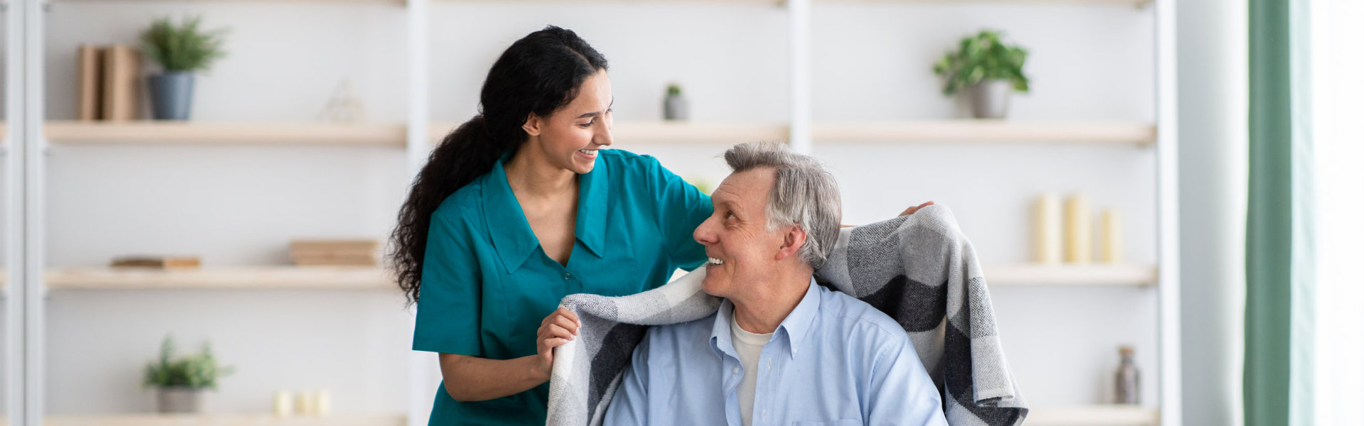 A female caregiver giving a coat to a senior man